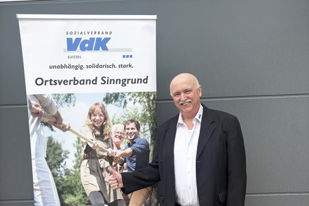 Das Foto zeigt den Ehrenamtlichen Anton Breitenbach vor einem Roll-up des VdK-Ortsverbands Sinngrund. Er l&auml;chelt. 