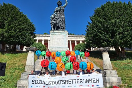 Teilnehmende des Aktionsb&uuml;ndnisses &bdquo;Gemeinsam f&uuml;r einen starken und zukunftsf&auml;higen Sozialstaat&ldquo; stehen in M&uuml;nchen vor der Bavaria in mehreren Reihen und halten ein gemeinsames Banner.