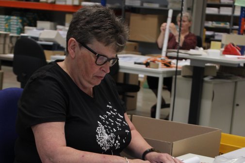 Eine Mitarbeiterin von Dimetria sitzt an ihrem Arbeitsplatz und rollt einen VdK-Wandkalender zusammen. 