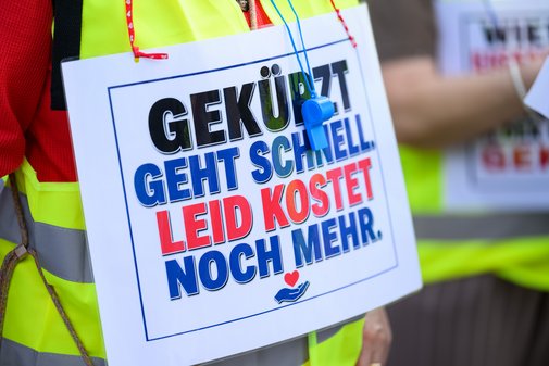 Nahaufnahme eines Schildes mit der Aufschrift 'GEK&Uuml;TZT GEHT SCHNELL LEID KOSTET NOCH MEHR' an einer Person mit Warnweste beim Demonstrationszug des VdK Bayern gegen Sozialabbau