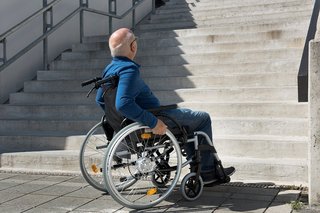 Ein Rollstuhlfahrer, der vor einer Treppe hält. 