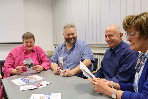 Vier Ehrenamtliche sitzen zusammen an einem Tisch. Zwei von ihnen sehen sich Brosch&uuml;ren &uuml;ber den VdK an.