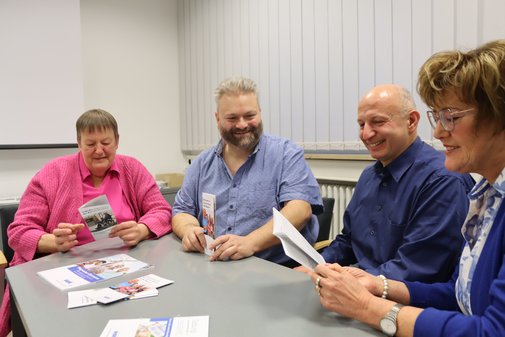Vier Ehrenamtliche sitzen zusammen an einem Tisch. Zwei von ihnen sehen sich Brosch&uuml;ren &uuml;ber den VdK an.