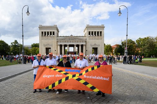 Die f&uuml;nf Mitglieder des Landesvorstand mit orangen M&uuml;tzen halten vor einem historischen Tor ein oranges Transparent mit der Aufschrift 'Gegen den Sozialabbau' und einem durchgestrichenen Schriftzug