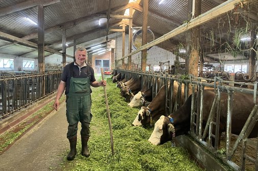 Georg Haug steht im Kuhstall des Biobauernhofs Leonhart. Er h&auml;lt eine Heugabel in der linken Hand. 