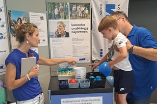 Auf dem Foto sieht man eine Mitarbeitende des Kreisverbands Rhön-Grabfeld (links) und einen Besucher mit seinem Sohn am Infostand.