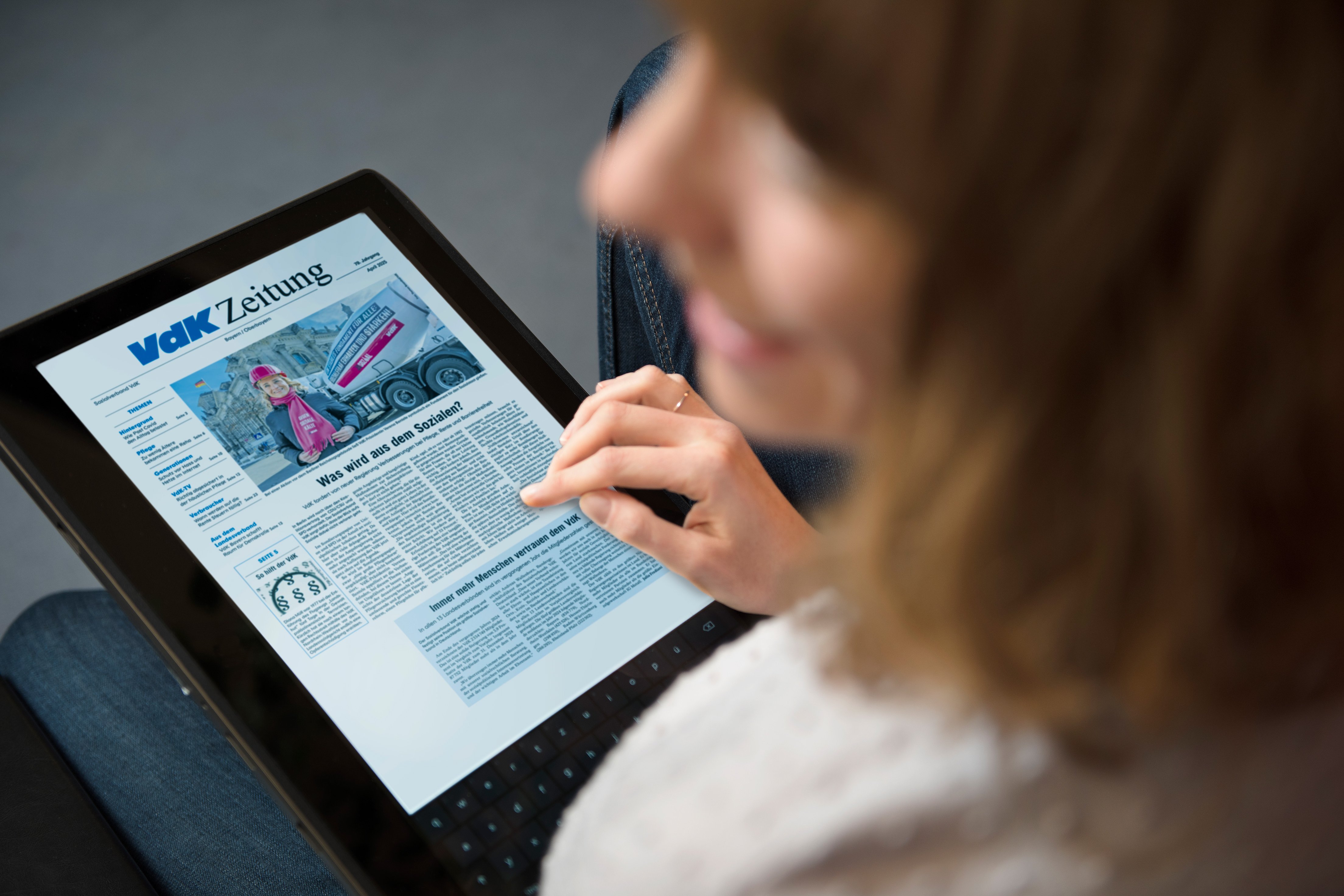 Eine Frau &acute;hat ein Tablet auf ihrem Scho&szlig;. Darauf sieht man eine Ausgabe der E-Zeitung.