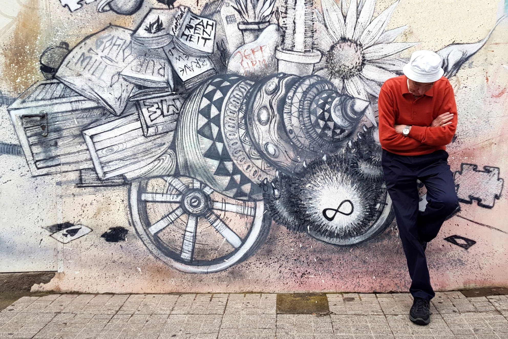 Auf dem Foto sieht man einen Mann, der vor einem Graffiti mit verschränkten Armen mit dem Rücken zur Wand lehnt. 