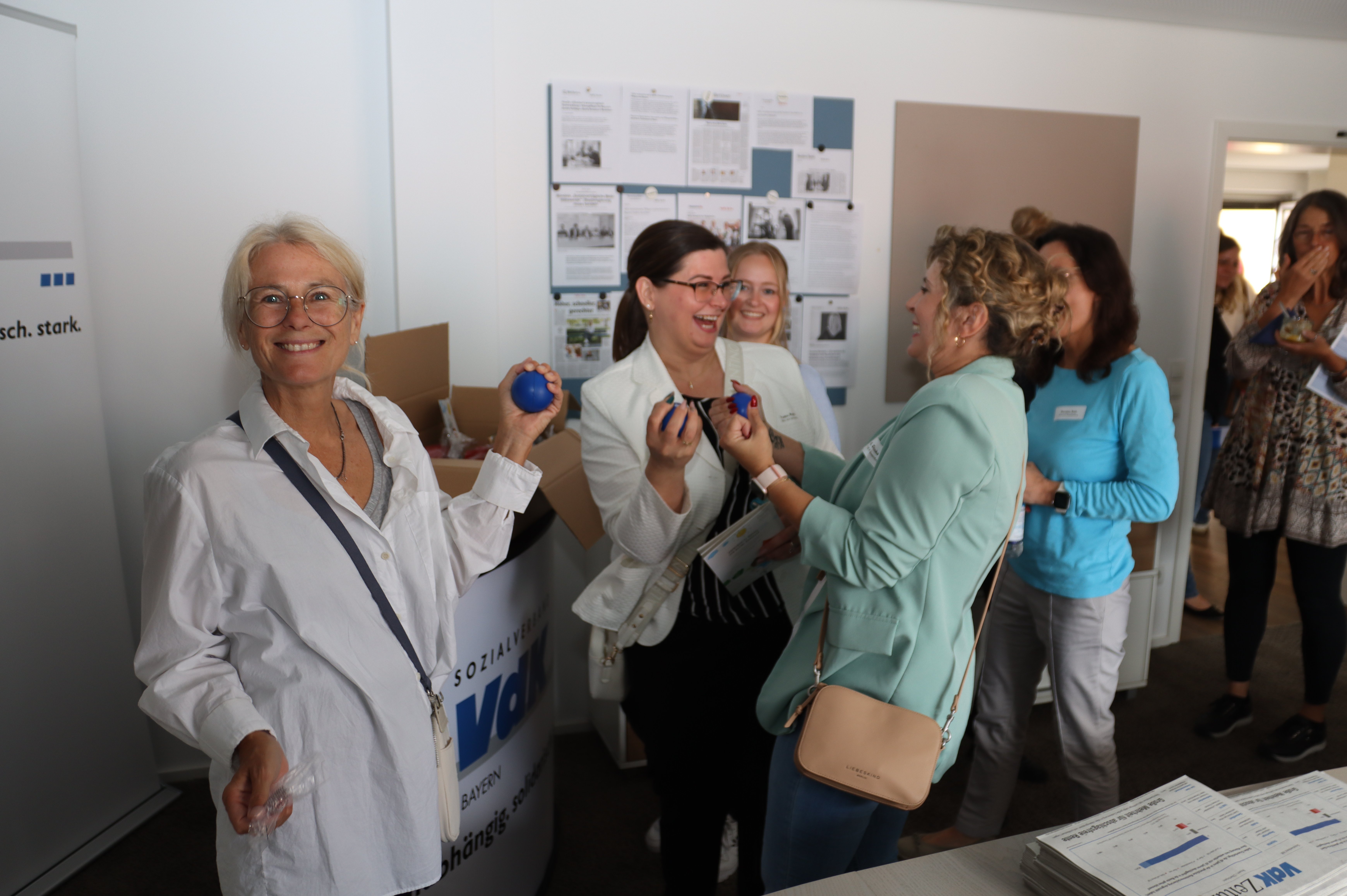 Das Foto zeigt fünf Mitarbeiterinnen des VdK bayern am Welcome Day. Sie probieren die Stressbälle des VdK aus und haben dabei Spaß. 