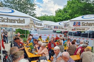 Auf dem Foto sieht man Mitglieder und Interessierte an den Bierbänken vor der Kreisgeschäftsstelle Hof sitzen. 