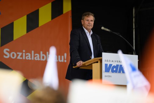 Stellvertretender Landesvorsitzender Hermann Imhof steht hinter einem Rednerpult mit dem Logo des Sozialverbands VdK Bayern und spricht auf einer Demonstration gegen Sozialabbau.