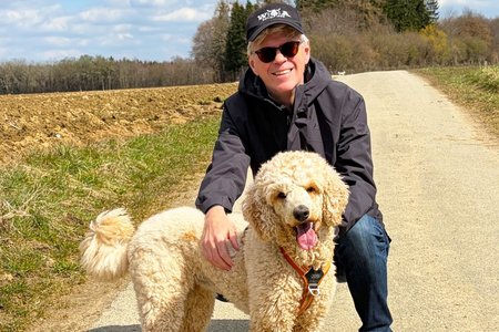 Gro&szlig;pudelh&uuml;ndin Afra und VdK-Landesgesch&auml;ftsf&uuml;hrer Michael Pausder stehen zusammen auf einem Feldweg. 