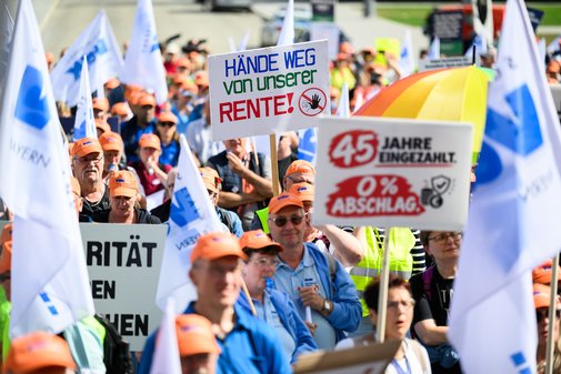 Demonstrationszug des VdK Bayern mit Menschen in orangen M&uuml;tzen, die Schilder mit Forderungen gegen Sozialabbau und f&uuml;r Rentenrechte halten