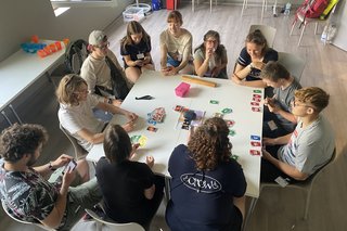 Das Foto zeigt Teilnehmenden der inklusiven Ferienfreizeit und ihre Betreuerinnen und Betreuer. Sie sitzen an einem Tisch und spielen ein Kartenspiel.