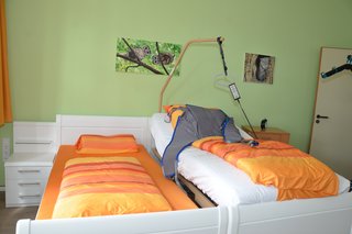 Auf dem Foto sieht man ein Doppelbett, dessen eine Hälfte in ein Pflegebett umfunktioniert wurde.