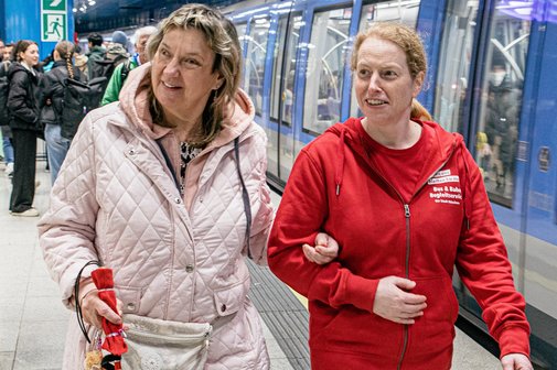 Eine Mobilit&auml;tsbegleiterin (rechts) begleitet eine Frau auf Kr&uuml;cken.