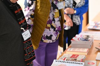 Auf dem Foto sieht man die Ehrenvorsitzende Ulrike Mascher und zwei Teilnehmerinnen der Landesfrauenkonferenz. Sie stehen vor einem Tisch, auf dem verschiedene Flyer und Broschüren liegen.
