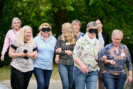 Eine Gruppe von Frauen geht nebeneinander. Manche Frauen haben Schlafmasken auf, sie werden von anderen Frauen am Arm gehalten.