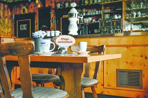 Auf dem Foto sieht man den Innenraum eines Lokals. Im Vordergrund sind zwei St&uuml;hle und ein Tisch. Auf dem Tisch stehen zwei Taschen und ein Schild mit "Pflegestammtisch". 