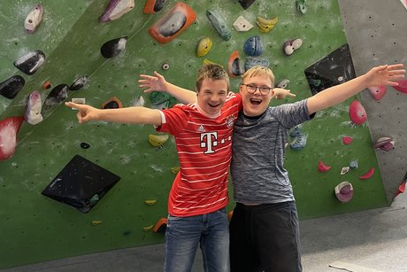 Das Foto zeigt Kinder mit Down-Syndrom in einer Boulderhalle. Sie halten sich in den Armen und lächeln in die Kamera. 