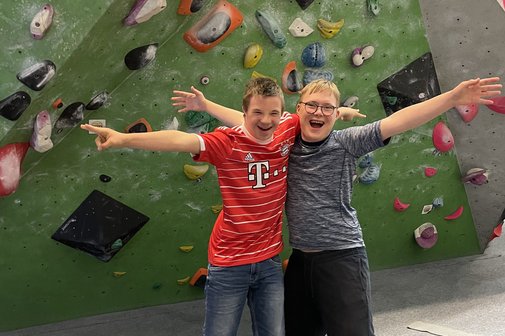Das Foto zeigt Kinder mit Down-Syndrom in einer Boulderhalle. Sie halten sich in den Armen und l&auml;cheln in die Kamera. 