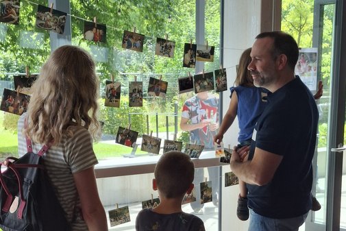 Zwei ehemalige Freizeitbegleiter*innen, die gemeinsam mit ihren eigenen Kinder alte Fotos der VdK-Freizeiten anschauen. 