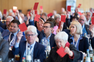 Auf dem Foto sieht man die Delegierten des VdK. Sie stimmen mit roten Karten in den Händen über das VdK-Zielbild 2030 ab., 