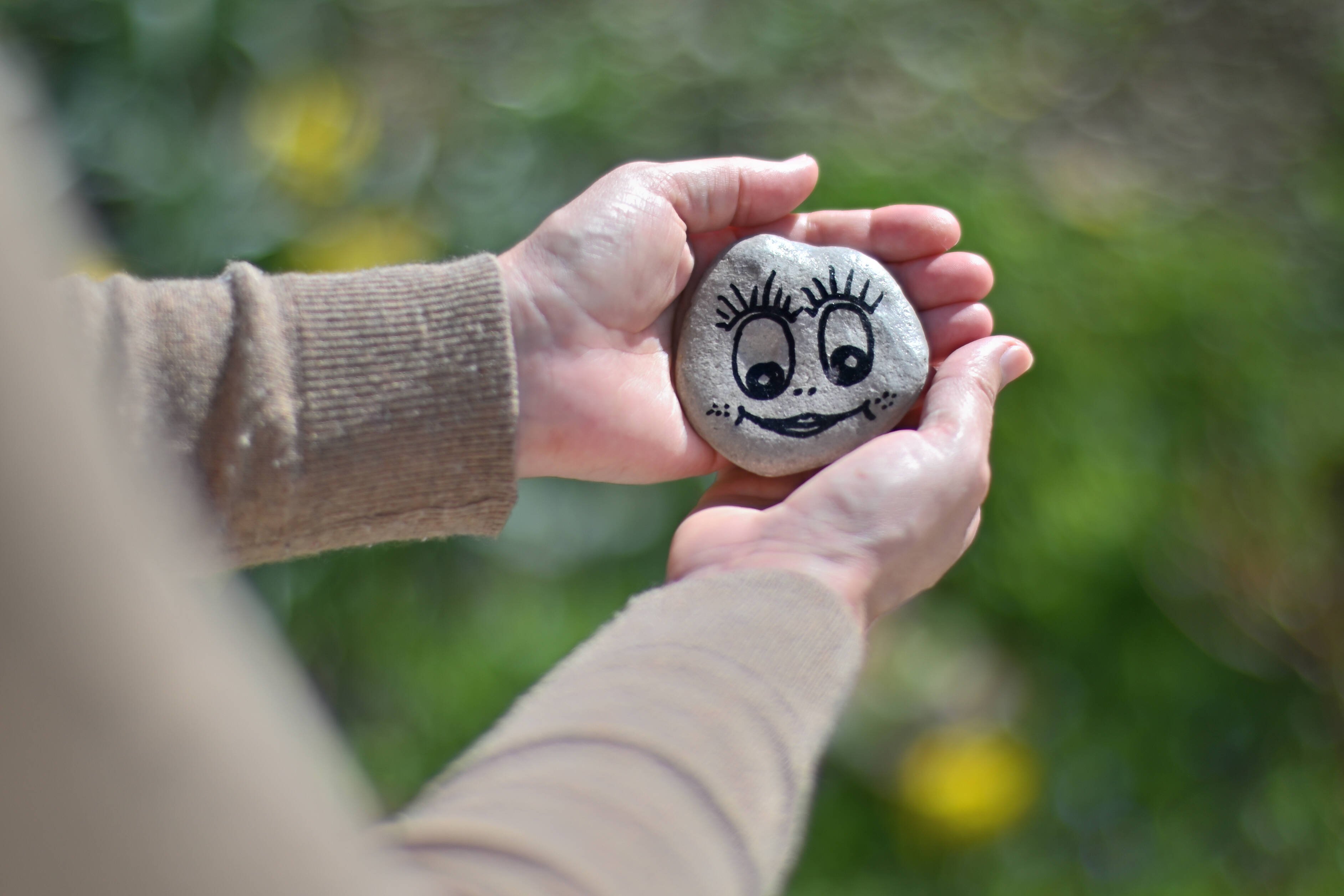 Jemand h&auml;lt einen grauen Stein in beiden H&auml;nden. Darauf ist mit schwarzem Stift ein l&auml;chelndes Gesicht gemalt. 