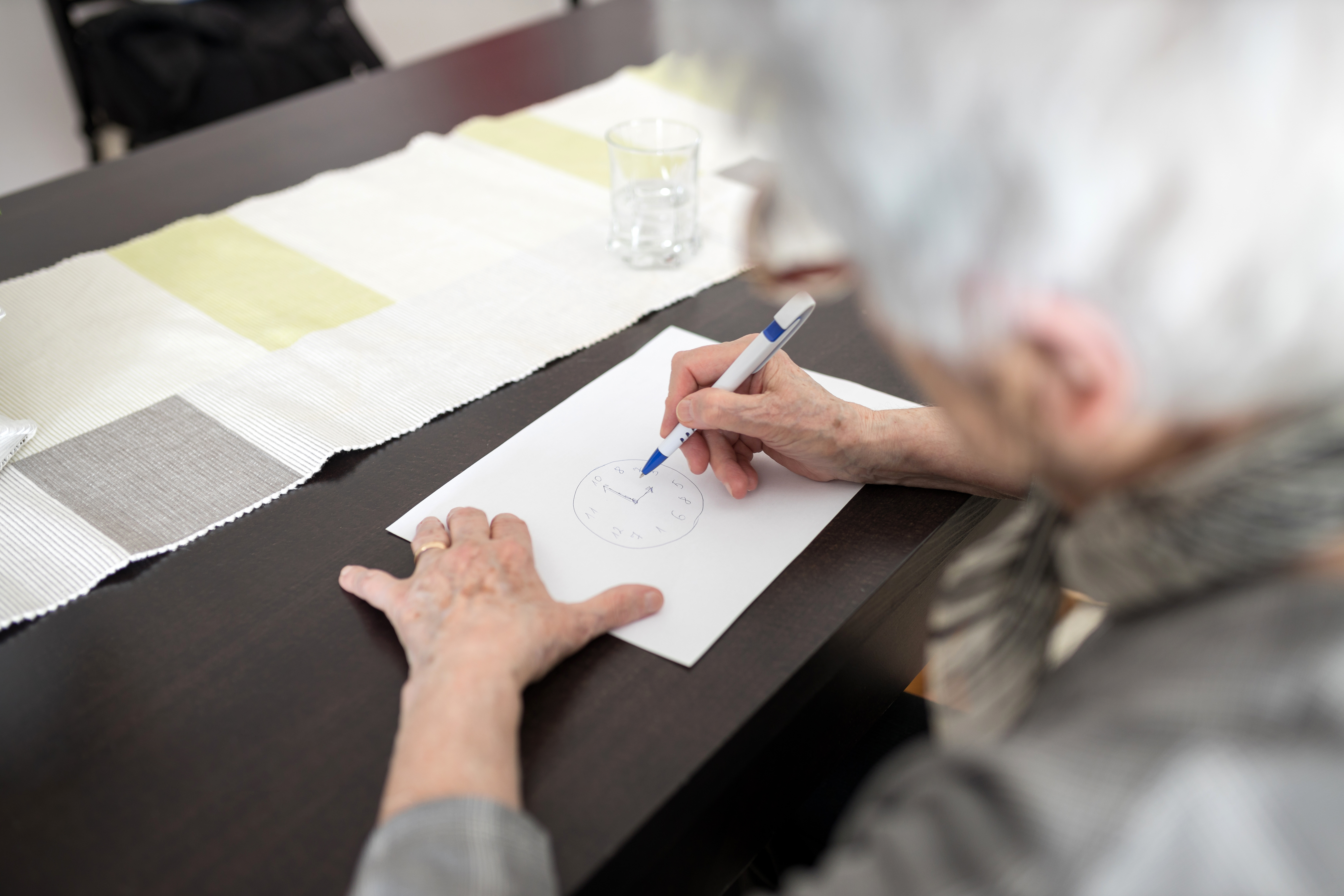 Eine ältere Dame macht hier einen speziellen kognitiven Test. Beim „Uhrentest“ versucht sie ein Ziffernblatt zu zeichnen.