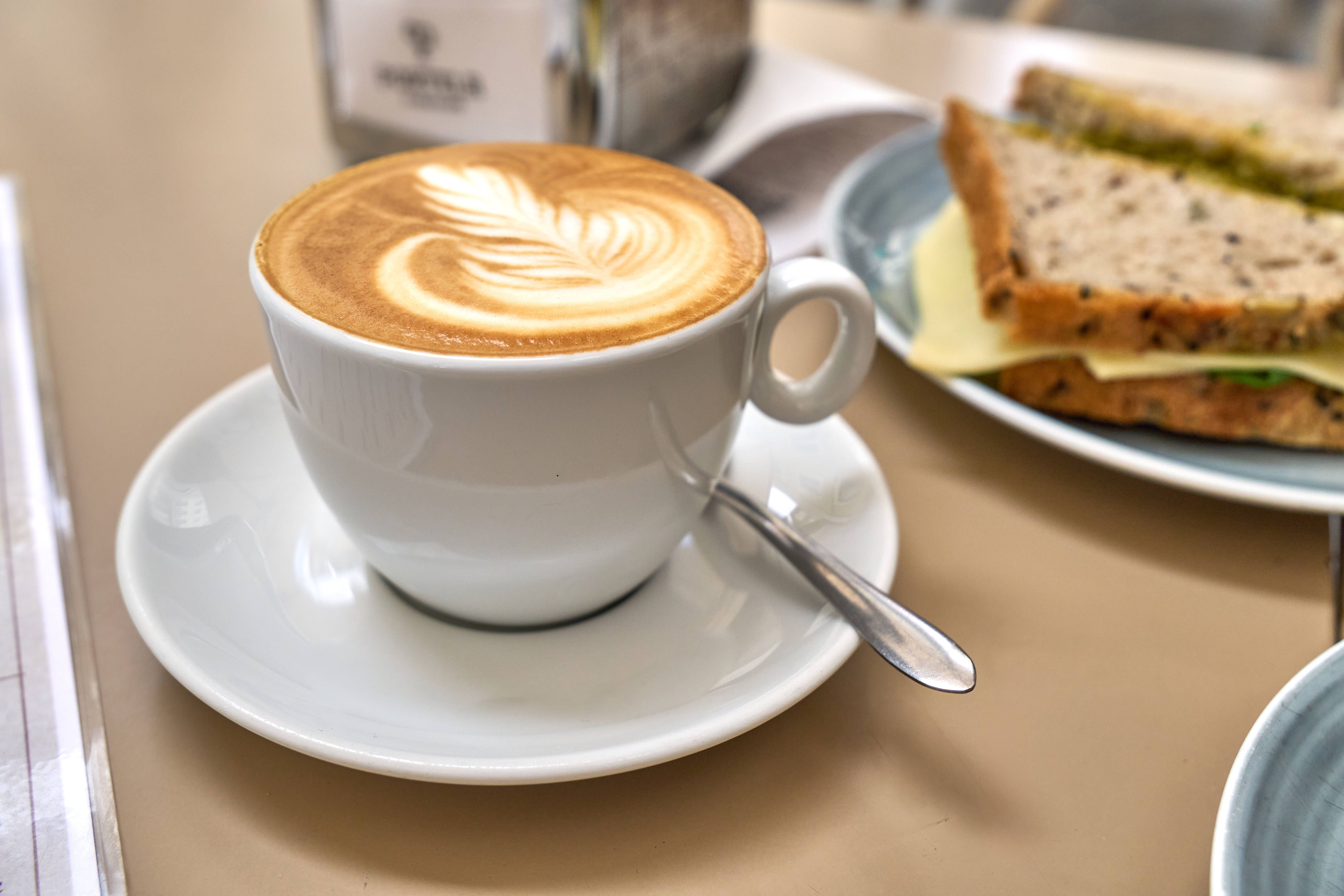 Eine Kaffeetasse (links) und ein belegtes Sandwich (rechts) stehen auf einem Esstisch.