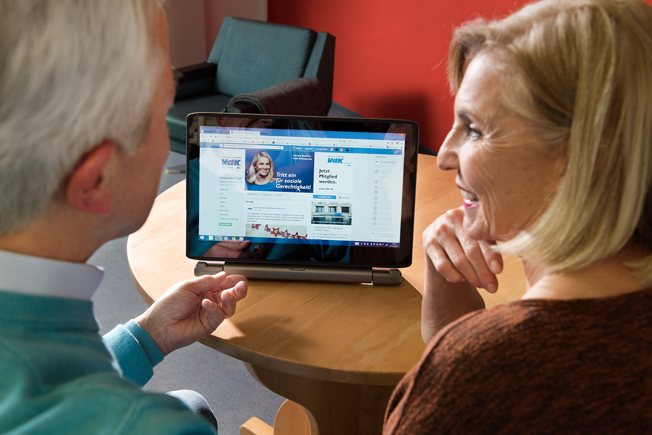 Ein &auml;lteres Paar am Computer, auf dem Bildschirm sieht man die Facebook-Seite des VdK Deutschland