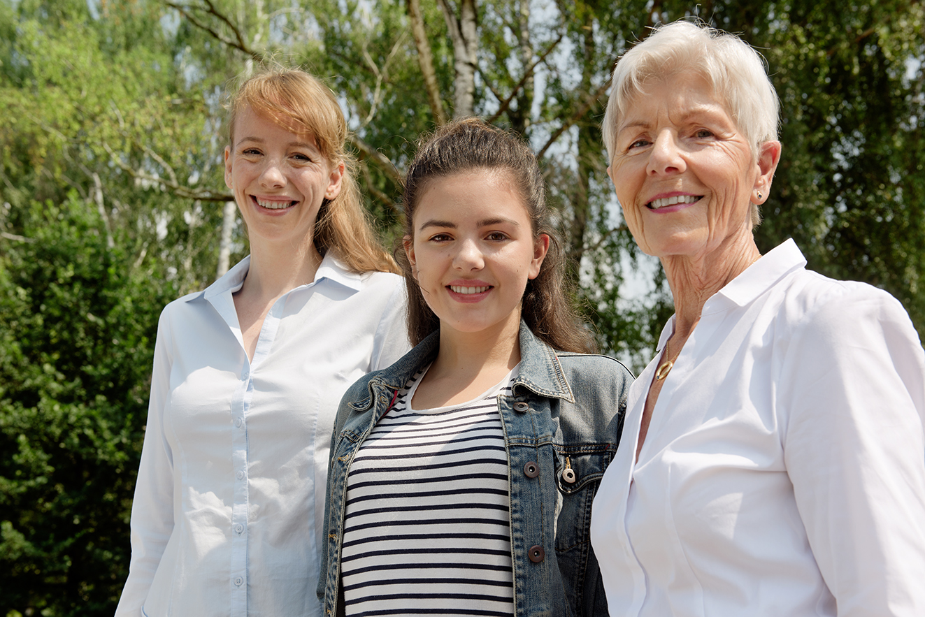 Drei Frauen lächeln gemeinsam in die Kamera: Eine jüngere, eine Teenagerin und eine ältere Frau.