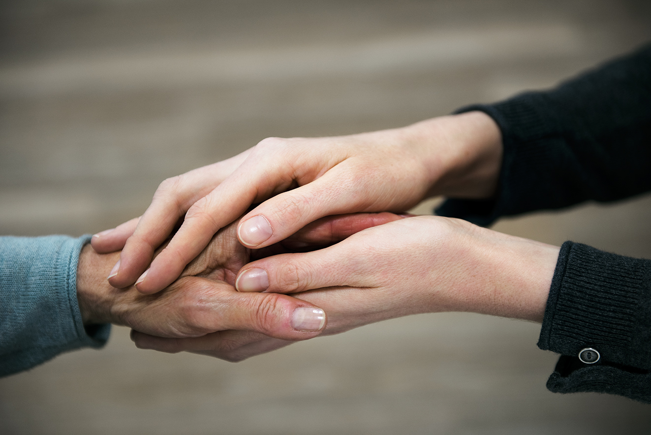 Die Hand einer j&uuml;ngeren Frau h&auml;lt die Hand einer &auml;lteren Frau in einer tr&ouml;stenden Geste.