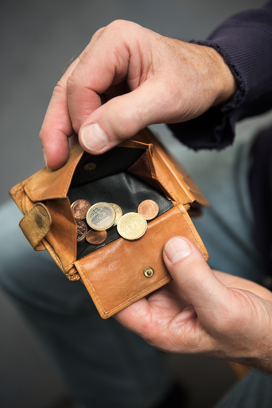 H&auml;nde eines Mannes halten eine Geldb&ouml;rse offen, darin befinden sich wenige M&uuml;nzen. 