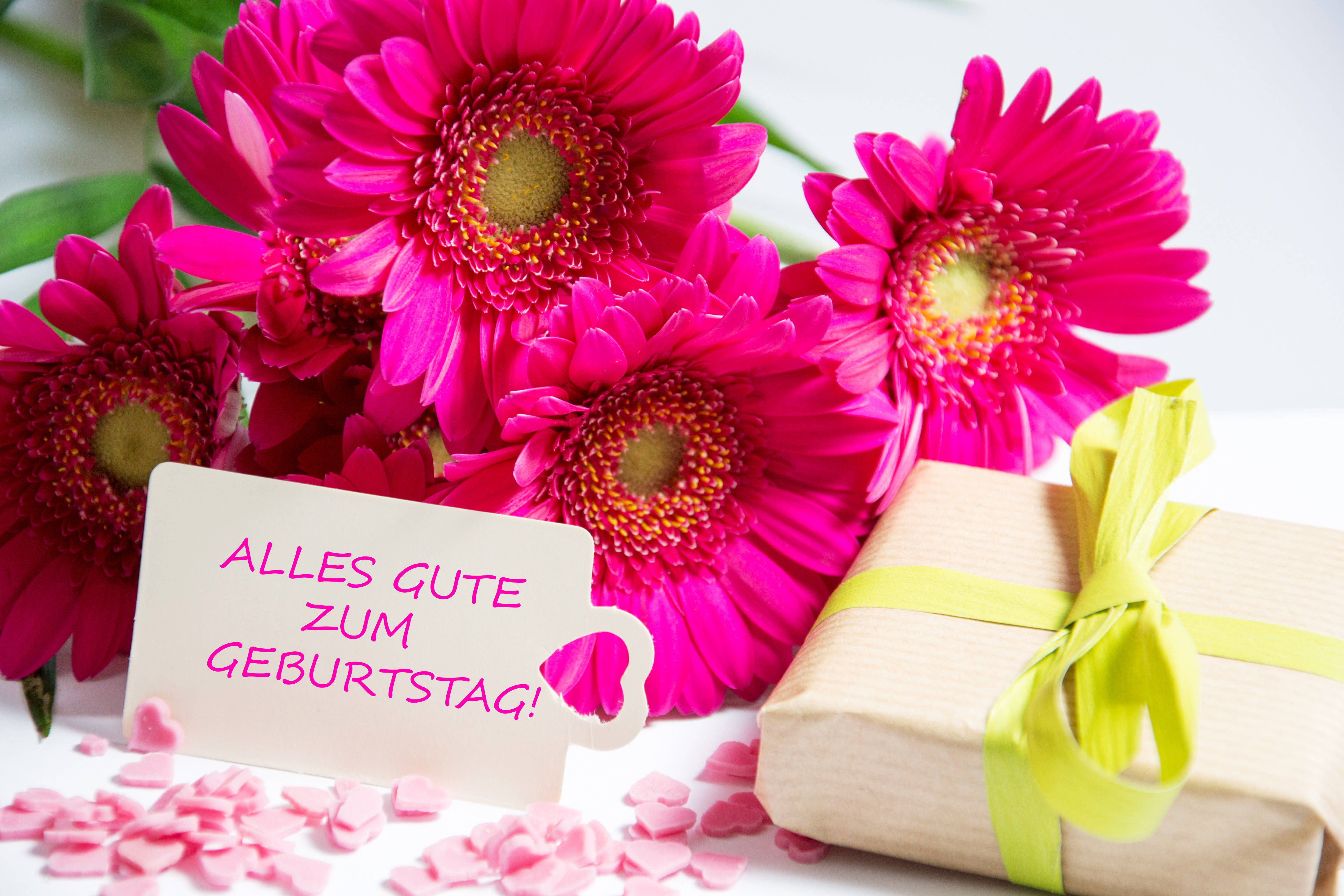 Geburtstagsgrüße : Ein Strauß Blumen mit einem Geschenk und einem Schild, auf dem steht: „Alles Gute zum Geburtstag!“.
