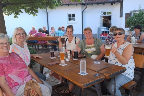 Fünf Frauen sitzen an einem Tisch im Biergarten und prosten sich zu.