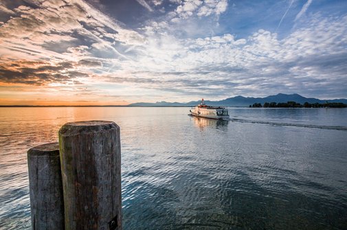 Auf dem Chiemsee bei Sonnenuntergang f&auml;hrt ein Schiff dem Horizont entgegen.