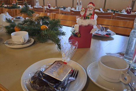Auf dem Bild sieht man einen Tisch mit Kaffeetassen, einen Nikolausstiefel, Tannenzweige mit Mandarinen dekoriert.