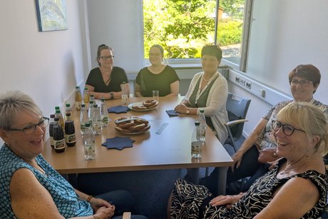 Besucher der Gesch&auml;ftsstelle sitzen mit ehrenamtlichen Mitarbeiterinnen am Tisch