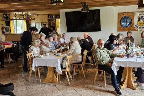 an 3 Tischen sitzen und sehen Personen, die sich unterhalten