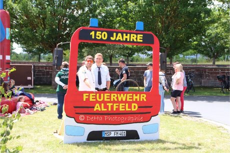 Bild zeigt ein Holzaufsteller als Feuerwehrauto mit zwei Personen die duch die Fensterscheibe schauen.