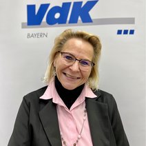 Auf dem Bild ist eine Frau mit blonden Haaren, rosa Bluse und schwarzer Jacke zu sehen