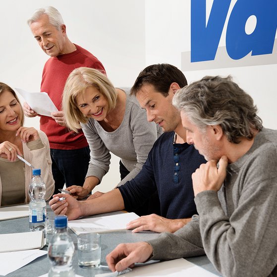 Verschiedene Menschen sitzen an einem Tisch, offenbar in einer Arbeitssitzung, an der Wand hinter ihnen ist ein gro&szlig;es VdK-Logo.