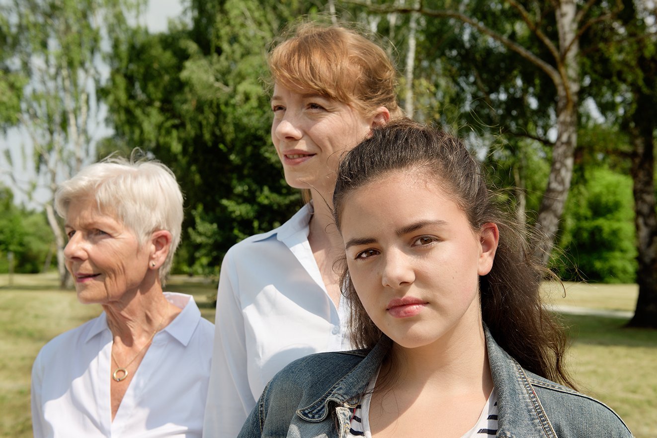 Drei Frauen - eine j&uuml;ngere Frau und eine &auml;ltere Frau blicken in die Ferne, eine Teenagerin blickt ernst in die Kamera. .