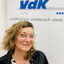 Auf dem Bild ist eine Frau mit kinnlangen gelockten blonden Haaren, Brille und schwarzem Oberteil zu sehen