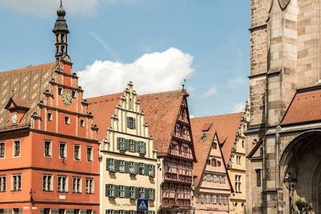 5 alte historische Fachwerkh&auml;user aneinandergereiht von links 2/3 des Bildes. Rechter Randstreifen ein Wehrturmtor; im Hindergrund blauer Himmel mit einer Wolke &uuml;ber den D&auml;chern von Fachwerkh&auml;usern.