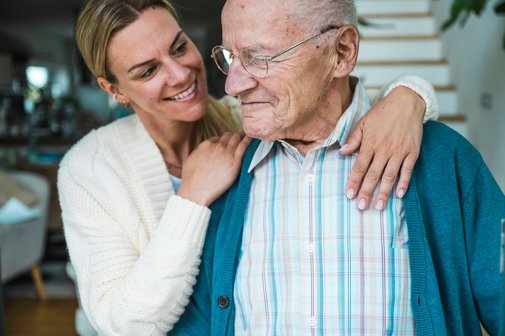 älterer Mann, der von einer Frau von hinten umarmt wird
