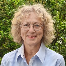 Frau Sch&ouml;sser, Schriftf&uuml;hrerin, tr&auml;gt eine Brille, hat blonde lockige Haare und tr&auml;gt eine blau wei&szlig; gestreifte Bluse.
