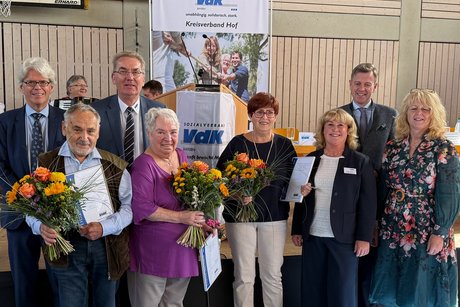 Die Geehrten stehen mit dem Landesgeschäftsführer, der Bezirksgeschäftsführerin, der Kreisgeschäftsführerin sowie dem Landrat vor der Bühne mit einem Blumenstrauß in der Hand