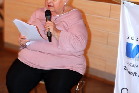 Bild005 Die kommissarische Ortsvorsitzende sitzt auf einem Stuhl und liest ein Gedicht vor